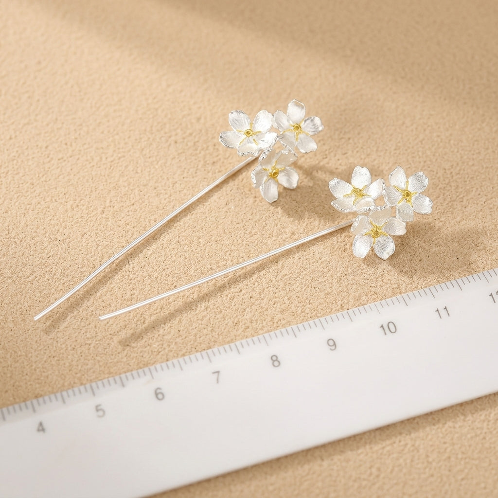 Close-up of artisan silver flower earrings with gold-plated highlights, showing the intricate texture of the three-flower vertical stud design.