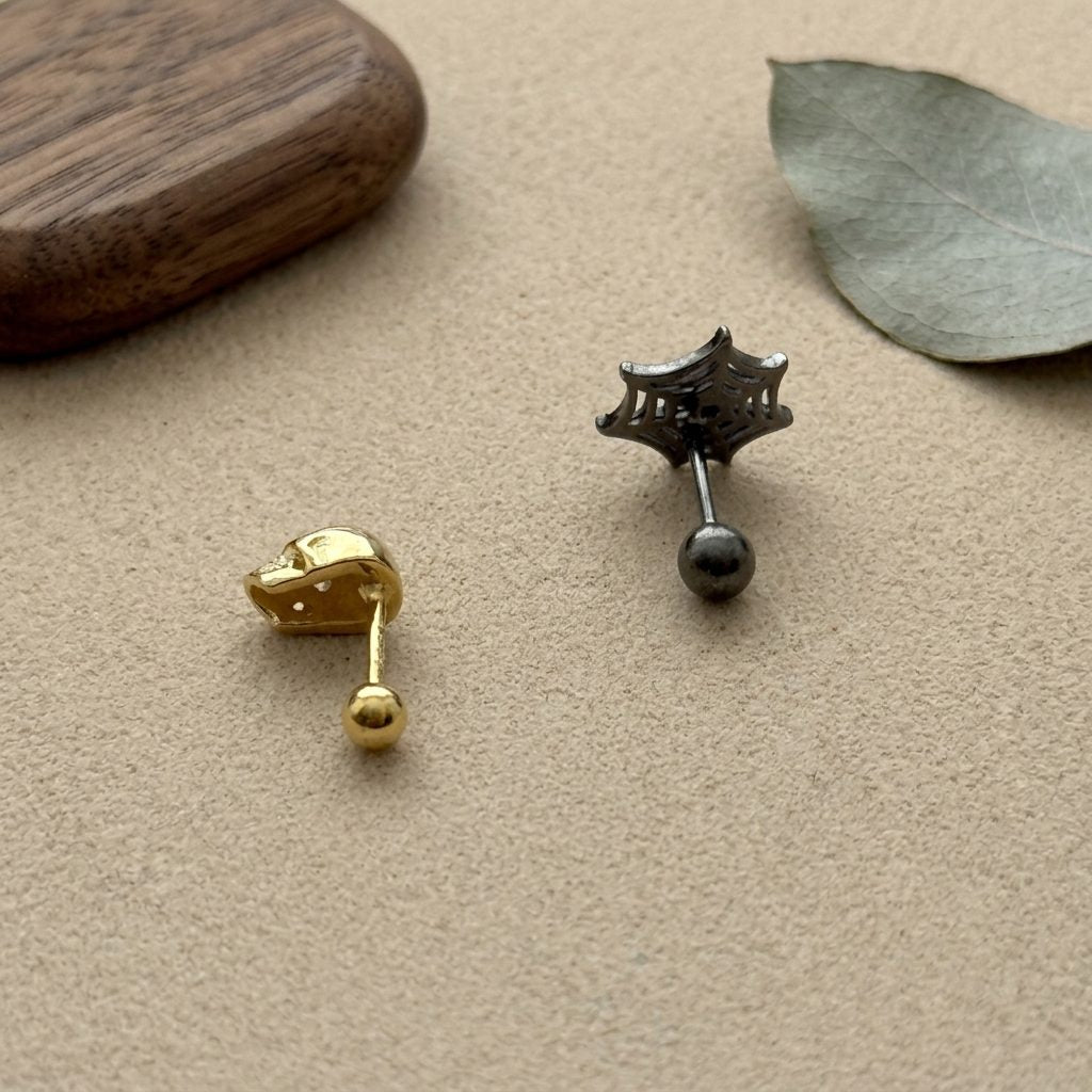 Gold plated skull stud paired with a black rhodium spiderweb stud, ball back closure