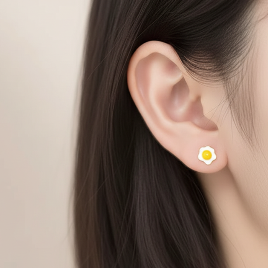 Close-up of a model wearing a petite fried egg stud earring in sterling silver and yellow enamel.