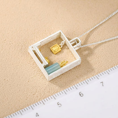 18kt gold-plated cat figurine and tropical leaf charm suspended within a fine silver square pendant.