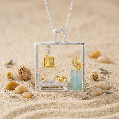 necklace featuring a gold-plated cat and cactus miniature scene inside a square silver frame